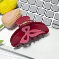Y2K style burgundy hair claw clip with pink bow design on a white desk background - Red