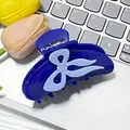 Dark blue acetate hair claw clip featuring a light blue bow accent on a desk setting - Blue