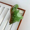 Close-up of a green dinosaur hair claw clip with marble texture on a white jewelry tray - Stegosaurus