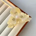 Detail der cremefarbenen Acetat-Haarklammer mit Blumenrelief, Steinen und zentraler Perle - Gelber Perlenakzent