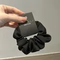 Detalle de un coletero de satén negro con pliegues suaves y etiqueta de marca en mano - Negro