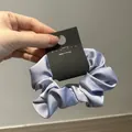 Detail of light purple satin hair scrunchie with silky luster and branded hang tag - Periwinkle Blue