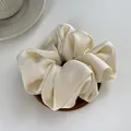 Close-up of cream satin scrunchie on wooden coaster showing smooth silk texture - L / Off White