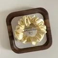 Close-up of a pale yellow satin scrunchie with soft silk texture on a wooden tray - Small / Yellow