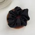 Detail of a black satin scrunchie with silky luster on a round wooden tray and white surface - M / Black