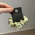 Detail of sage green satin scrunchie on display card showing silky fabric texture - Green