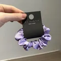 Detailed view of a purple silk satin scrunchie with soft pleats on a display card - Purple
