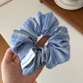 Blue and white striped scrunchie with embroidery and brand label held by hand - Dark Blue