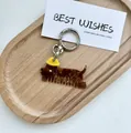 Dettaglio di un pettine portachiavi in acetato a forma di bassotto su un vassoio di legno - Cane col cappello