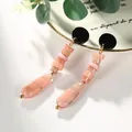 Détail de boucles d'oreilles à pompons en acrylique rose et noir sur un plateau - Rose Foncé Veiné de Noir (EH00010)