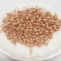 Gros plan de clous d'oreilles boules en or rose en vrac sur un plateau en céramique - Orientation Horizontale (Petit) / Or rose