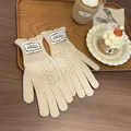 Close-up of cream knit gloves with diamond cutouts and ruffled cuffs on wood tray - Cream Rice