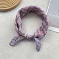 Détail d'un foulard à carreaux violets avec un design noué et des motifs floraux légers - Rose