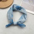 Close-up of light blue floral cotton linen square scarf tied in a bow on a white surface - Azure Blue