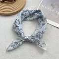 Detail view of light blue floral silk scarf knotted on a white textured fabric background - White Cherry Leaf