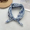 Detailed close-up of blue and white floral silk scarf tied in a knot on a textured surface - White Rendered Oil Spots