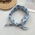 Detailed view of lightweight blue floral silk scarf tied in a knot on soft white texture - White Flower