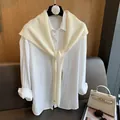 Dettaglio dello scialle in maglia di lana crema annodato su una camicia bianca - Bianco Sporco