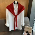 Dettaglio scialle in lana rossa annodato su camicia bianca su sfondo di legno naturale - Rosso