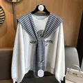 Detailed view of striped knit shawl layered over a grey sweatshirt with university print - Gray