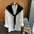 Dettaglio di uno scialle in lana nera lavorata a maglia sopra una camicia bianca con fibbie - Nero
