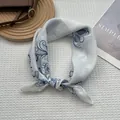 Gros plan d'un foulard carré en soie aux motifs de branches bleues noué avec élégance - Exotique Blanc / 70x70cm
