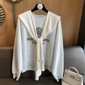 Detail eines cremeweißen Strickschals kombiniert mit einem grauen College-Sweatshirt - Creme