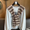 Detail of a brown striped knit shawl layered over a grey Northwestern sweatshirt - Camel