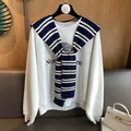 Close-up of navy striped knit shawl over a grey college style sweatshirt with logo - Navy Blue