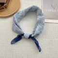 Carré de soie bleu à motif cachemire noué sur un fond en tissu texturé blanc éclatant - Paisley Bleu / 70x70cm