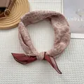 Détail d'un foulard en soie à motif paisley rose poudré et beige noué sur un plateau - Paisley Café / 70x70cm