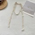 Dettaglio macro della cravatta in pizzo beige con trama fine su tessuto a nido d'ape bianco - Griglia