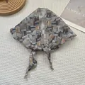 Détail d'un foulard triangulaire en soie avec motifs géométriques et bords à volants - Petit bâton en bois