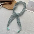 Detail of light blue floral skinny scarf featuring delicate tassels on a grid texture backdrop - Light Blue with White Floral (2)