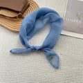 Light blue silk-like square scarf tied in a bow with golden metal tag on white fabric - Lake Blue