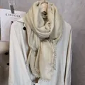 Elegante bufanda de encaje champán con ribete de pompones colgada en un perchero - 180x90cm / Blanco Roto