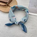 Detail of light blue floral silk scarf featuring refined rolled edges and knotted style - Blurred Flower Blue