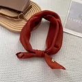 Close-up of caramel faux silk square scarf with a circular metal pendant on textured fabric - Burgundy