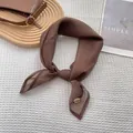 Detail view of a dark brown silk scarf with fine stitching and a metal brand tag - Coffee