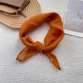 Close-up of bright orange silk scarf tied in a bow with metallic logo on waffle background - Orange