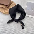 Detail view of a black silk scarf with a gold oval pendant on a white waffle texture cloth - Black