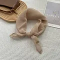 Detail of champagne silk scarf with golden logo tag on white waffle texture fabric - Khaki