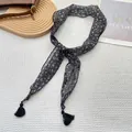 Dettaglio della sciarpa floreale stretta con nappe nere su una superficie testurizzata - Nero con Floreale Beige (21)