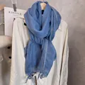Close-up of light blue cotton linen scarf with delicate lace trim hanging on a beige coat - Denim Blue