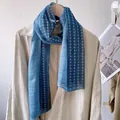 Detail view of lightweight blue scarf with white polka dots draped on a beige trench coat - Blue