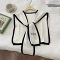 Close-up of white knitted shawl with black trim and brand label on a wooden hanger - White