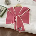 Detail of pink knit shawl showing fabric texture and woven brand label on white bedding - Peach Pink