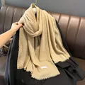 Dettaglio di una sciarpa in lino champagne plissettata con frange su cappotto nero - Increspature ananas / Cachi