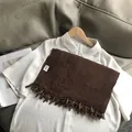 Detail van de donkerbruine sjaal met ribbeltextuur en fijne franjes aan de randen - koffiekleur