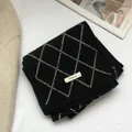 Detailed view of the 100% wool label on a black and beige diamond pattern knit scarf - Black
